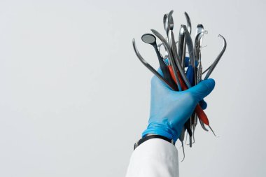 The dentists hand in a blue glove holds bunch of dental instruments, dental mirror, tweezers, probe hook. Advertising of dentistry and dental services