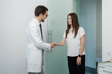 Side view of a cheerful male dentist in medical uniform welcomes his patient and shaking hands in dental office