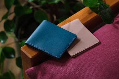 Two colored genuine leather wallets with blank space to place a logo or text. Wallets lying on a purple sofa indoors