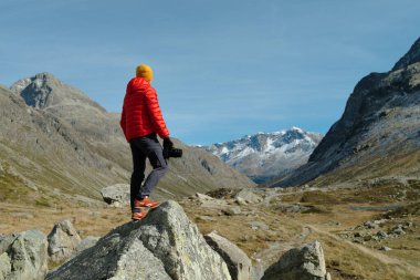 Back view of a tourist man in red jacket and camera standing with a view on Julier Pass, Switzerland clipart