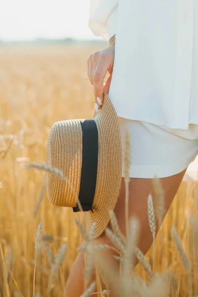 Closeup shot of female hand holding straw hat in a wheat field on a sunny summer day. The concept of outdoor recreation, a trip to the village