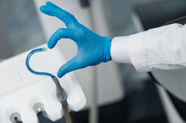 Saliva ejector and a hand in a disposable glove symbolize love in dentistry. Hand in a blue glove with blue saliva ejector. Heart symbol.