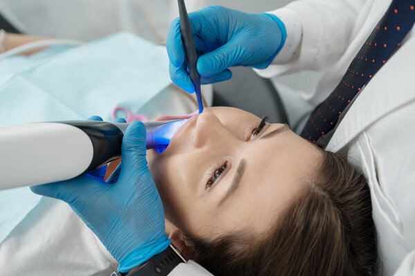 Closeup of female patient in dental chair on a procedure of intraoral digital scan of her teeth. Modern 3D dental scanner