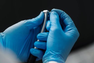 A close photo of a hand of a dentist who holds a dental diamond bur in the turbine stainless handpiece. Closeup shot on black background