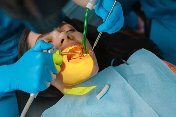 Dentist uses photopolymer lamp to cure carious teeth of the female patient in dentist office