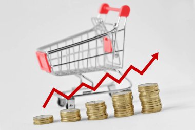 Pile of coins with arrow and shopping cart on the background - Concept of increasing purchases