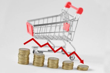 Pile of coins with arrow and shopping cart on the background - Concept of decreasing purchases