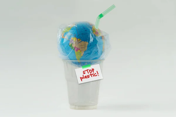 Earth globe in a plastic bag with straw on plastic glass and the written Stop plastic! - Concept of ecology and stop plastic pollution