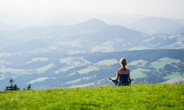Genç bir kadın dışarıda meditasyon yapıyor.
