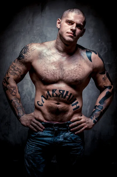 Мускулистый молодой человек со многими татуировками, позирующий на сером фоне — стоковое фото