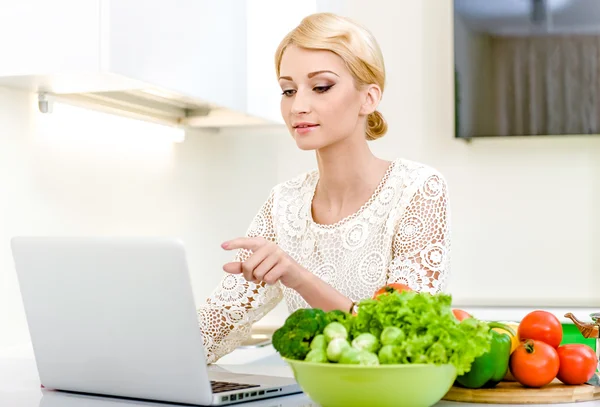 Mujer buscando una receta en el ordenador en la cocina — Foto de Stock