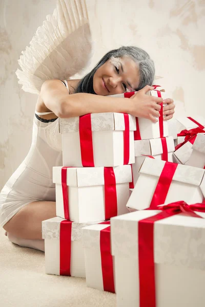 Schöne junge Frau als Engel mit Haufen von Geschenkboxen drinnen — Stockfoto