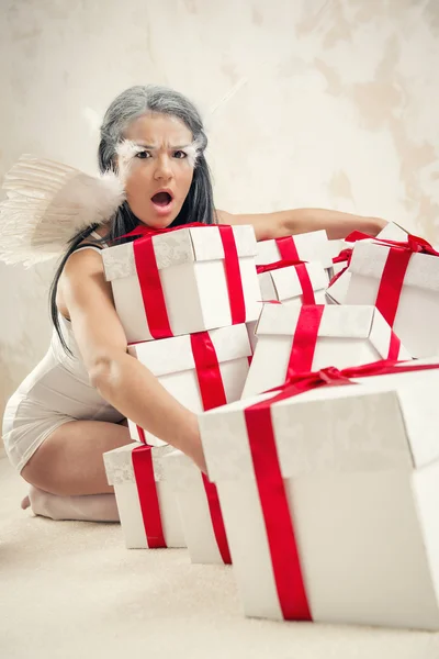 Schöne junge Frau als Engel mit Haufen von Geschenkboxen drinnen — Stockfoto