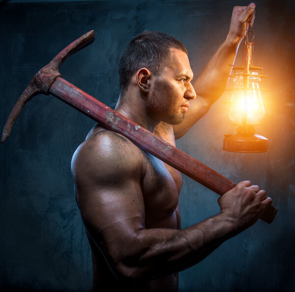 Muscular man holding pickaxe and oil lamp