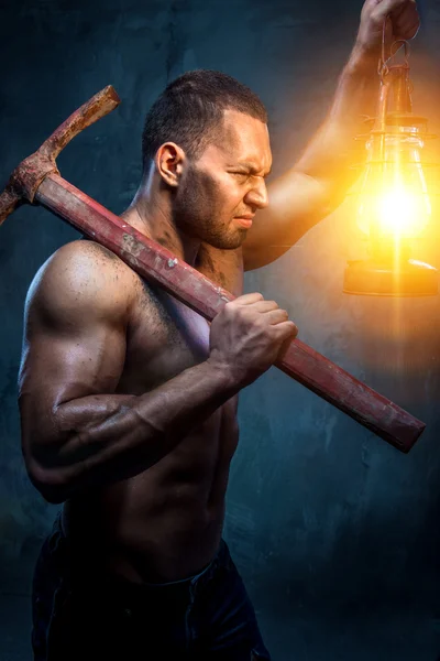 Homem muscular segurando picareta e lâmpada de óleo — Fotografia de Stock