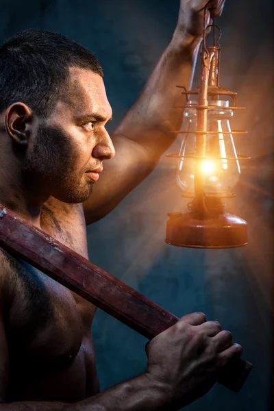 Muscular man holding pickaxe and oil lamp — Stock Photo, Image