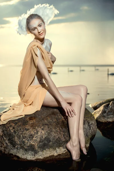 Mladá krásná žena jako Labutí pózuje na pláži při západu slunce — Stock fotografie
