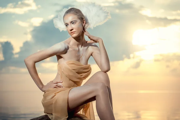 Jonge mooie vrouw als zwaan poseren op het strand bij zonsondergang — Stockfoto