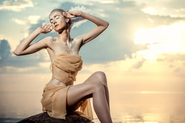 Молодая красивая женщина, как лебедь, позирует на пляже на закате — стоковое фото