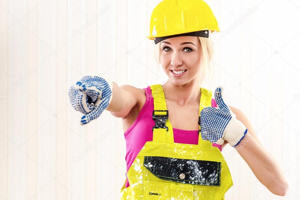 Woman in coverall and hard hat showing thumbs up indoors