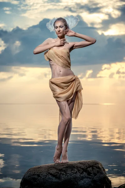 Jonge mooie vrouw als zwaan poseren op het strand bij zonsondergang — Stockfoto