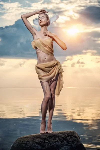 Mladá krásná žena jako Labutí pózuje na pláži při západu slunce — Stock fotografie