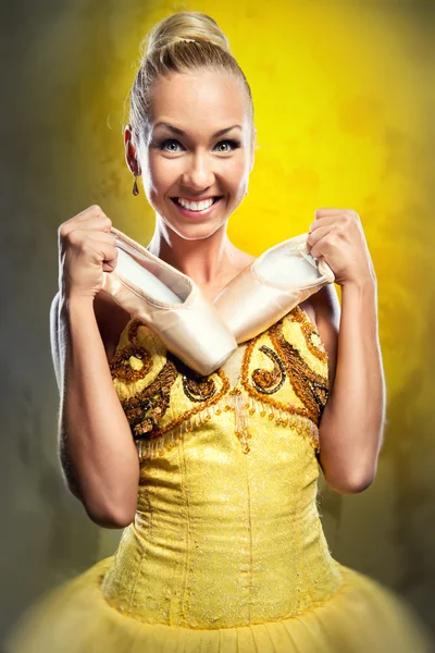 Smiling ballerina in yellow tutu holding pointe shoes — Stock Photo, Image