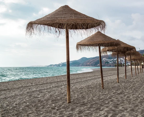 Slaměné slunečníky na opuštěné pláži. Nerja, Španělsko — Stock fotografie