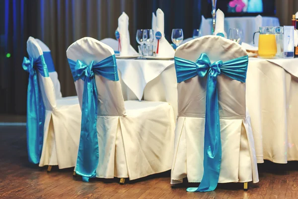 Bílé svatební židle zdobené modrými luky v restauraci — Stock fotografie