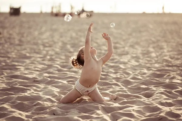 Schattige babymeisje spelen met zeepbellen op het strand — Stockfoto