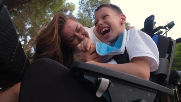 愛情のある母親は絆を感じ 頬にキスをするのが大好き彼女の小さな9S息子と脳性麻痺は車椅子の屋外に座っています 無条件の母親は愛の概念 — ストック動画
