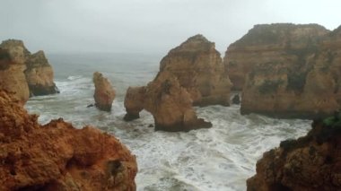 Uçan insansız hava aracı bakış açısı azgın okyanus ve Ponta da Piedade burnu. Kireçtaşı kıyı şeridi boyunca sarı uçurumlar, Lagos kasabası, Portekiz 'in en ünlü turistik merkezi.