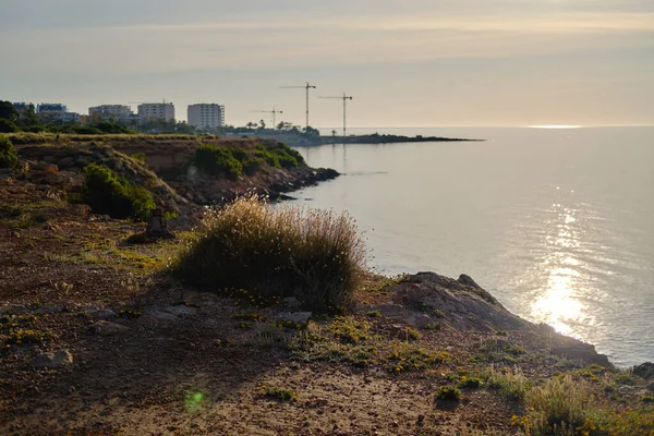 落日余晖中普莱马海岸线的岩石 平静的地中海和摩天大楼构成的城市天际线 科斯塔布兰卡 阿利坎特省西班牙 — 图库照片
