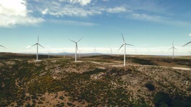 Drone bakış açısı yel değirmenlerinin türbinlerini hareket ettiriyor. Rüzgâr enerjisini elektriğe çevirir. Panoramik görüntü, ekilmiş tarım arazileri güneşli yaz gününde mavi bulutlu arka planda. Avrupa, İspanya