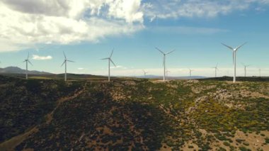 Drone bakış açısı yel değirmenlerinin türbinlerini hareket ettiriyor. Rüzgâr enerjisini elektriğe çevirir. Panoramik görüntü, ekilmiş tarım arazileri güneşli yaz gününde mavi bulutlu arka planda. Avrupa, İspanya