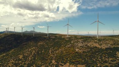 Drone bakış açısı yel değirmenlerinin türbinlerini hareket ettiriyor. Rüzgâr enerjisini elektriğe çevirir. Panoramik görüntü, ekilmiş tarım arazileri güneşli yaz gününde mavi bulutlu arka planda. Avrupa, İspanya