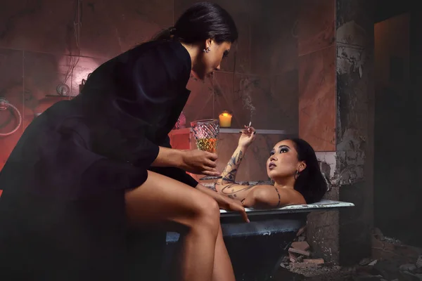 バスルームでタバコとガラスのポーズをとっている2人の若い美しい女性 ファッションと美しさのコンセプト — ストック写真