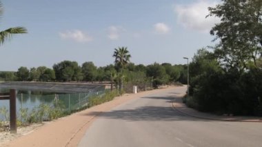 Güneşli yaz günlerinde gölet yolunu ve konut binalarını gösteren hareketli bir kamera, hiç insan yok. İspanya, Costa Blanca