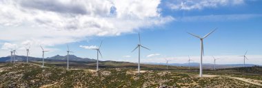 Drone bakış açısı yel değirmenlerinin türbinlerini hareket ettiriyor. Rüzgâr enerjisini elektriğe çevirir. Panoramik görüntü, ekilmiş tarım arazileri güneşli yaz gününde mavi bulutlu arka planda. Avrupa, İspanya