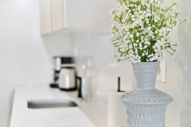 Mutfak tezgahında gri vazoda şirin, beyaz çingene çiçeklerinin yakın görüntüsü, insan yok. Modern oda arkaplanı