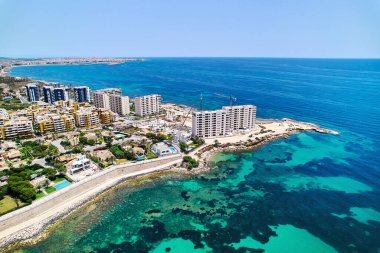 Punta Prima sahilinde yüksek binalar, güneşli bir yaz gününde Akdeniz 'in turkuaz körfezi boyunca uzanan patika. Costa Blanca, Alicante vilayeti. İspanya. Seyahat ve tatil kavramı