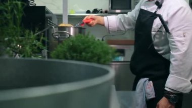 Önlüklü İspanyol şef restoranda ayakta duruyor spagetti spatulasını tavada makarna karıştırıyor, ana yemek tabağını halka açık bir yerde hazırlıyor. Profesyonel meslek, aşçılık.