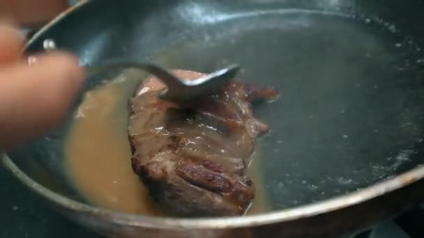 关闭不明厨师用勺子把汤倒在煎锅里的一块肉上 浸泡在锅里 在餐馆厨房里准备菜 — 图库视频影像