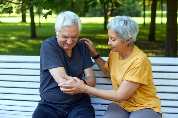 During morning sportive stroll or making exercises in a park, elderly 60s man got injured his shoulder gripping arm sit in bench with caring disappointed wife. Traumas, injures of older people concept
