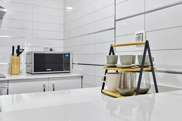 Cozy light domestic kitchen interior, counter top with microwave, appliances, coffee cups, tea mugs, no people. Modern home concept