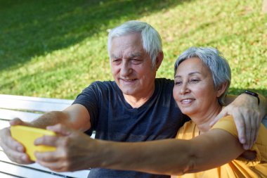 Mutlu kıdemli eşler selfie çekerler yaz parkında bankta otururlar. Gri saçlı çift cep telefonu ekranına bakar dışarıyı arar modern teknolojiyi kullanır, internette eğleniriz. Dışarıda vakit geçiririz.