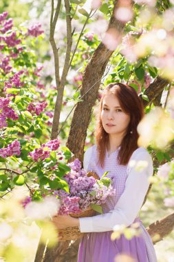 Çiçekli leylak çiçekli bir bahçede, klasik elbiseli, güzel kızıl saçlı bir kadın.