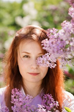 Çiçekli leylak çiçekli bir bahçede, klasik elbiseli, güzel kızıl saçlı bir kadın.