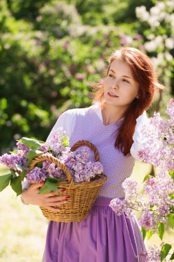 Çiçekli leylak çiçekli bir bahçede, klasik elbiseli, güzel kızıl saçlı bir kadın.
