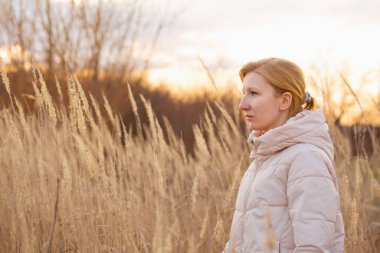 Genç sarışın kadın, batan güneşin altında yalnız başına yürüyor.